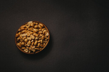 top view of wooden bowl full of peanuts on black background