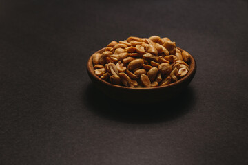 Small bowl of organic, salted peanuts placed on black backgroud