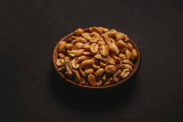 Top view of salted peanuts placed in a wooden bowl on black background in the middle of the frame