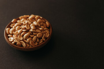Top view of salted peanuts placed in wooden bowl on black backgroud