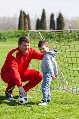 Obraz premium Father with his little son playing football, soccer in the park. Father teaches his son