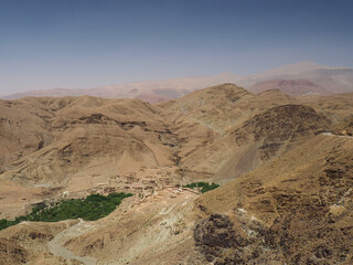 Oasis in the middle of desert, seen from above. Plantation of date trees palm and cultivation other food plant. Island of vivid green between rough environment of lifeless deser hills. Photo taken in 