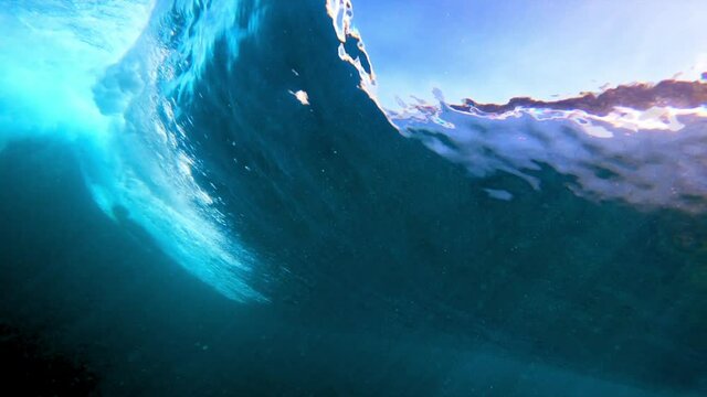 Dramatic underwater of a large ocean wave rolling and breaking, with dark blue water and illuminated bubbles - Oahu, Hawaii