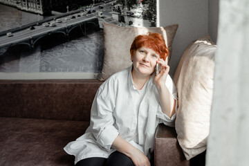 grandmother with red hair sitting on the couch talking on a mobile phone
