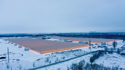 Aerial side view of large industrial greenhouses for growing plants in winter. light pollution. winter day at sunset. Flying along modern plantation glasshouse area. growing plants vegetables flowers