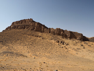 Fototapeta na wymiar Ancient fortress on the top of the hill surrounded by the desert sand. Grey stones and grey ancient wall on the yellow sand, clear blue sky. 