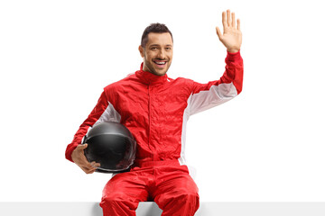 Male racer in a red uniform sitting on a panel and waving