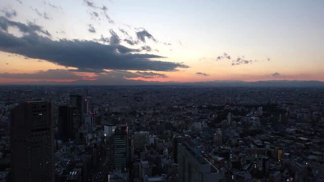TOKYO, JAPAN : Aerial high angle sunset CITYSCAPE of TOKYO. View of dramatic clouds and buildings around Shibuya. Japanese city life and metropolis concept. Long time lapse zoom out shot dusk to night