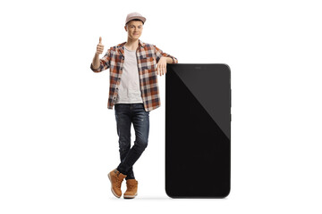 Full length portrait of a male teenager leaning on a big smartphone with blank screen and showing thumbs up