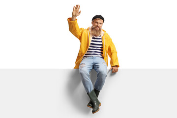 Bearded fisherman with a yellow rain coat sitting on a panel and waving