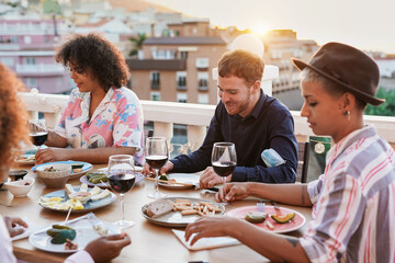 Young multiracial people enjoy dinner outdoor on patio at sunset - Concept of friendship