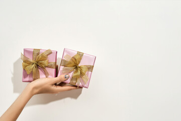 Gift for 8 March. Female hand holding two small wrapped gift boxes with golden bows against white background, copy space for text