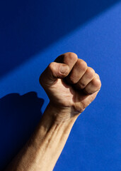 Swarthy rough mans hand with clenched fist on blue background. Cesar Chavez Day concept.