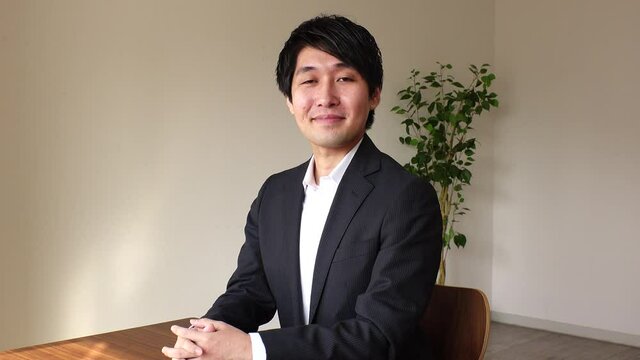 Young Asian (Japanese) business man wearing a black suit at the office. One person, black hair, looking at the camera. Office worker or company employee. Job interview concept shot.