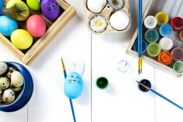 Easter light holiday concept. Eggs, paints and brushes on a white wooden table. Easter background.