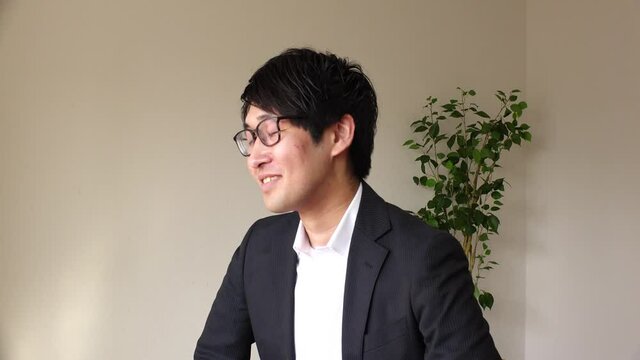 Young Asian (Japanese) business man wearing a suit at the office. One person, black hair, looking at the camera, laughing and smiling. Office worker or company employee. Job interview concept shot.