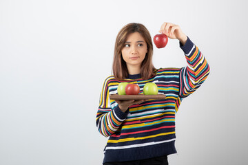 Adorable young girl in casual clothes showing red apples over white wall