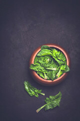 Fresh spinach leaves in a wooden bowl on a dark rustic background. Fresh vitamin rich food concept, low key