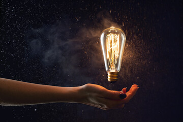 hand holds in the air a burning vintage light bulb without wires - obrazy, fototapety, plakaty