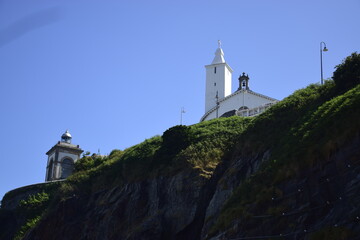 Fototapeta na wymiar Faro y torre de una iglesia en lo alto de un acantilado de una aldea pesquera y turística de la costa cantábrica española