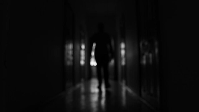 Blurred silhouette of an unknown man walking in the dark corridor.