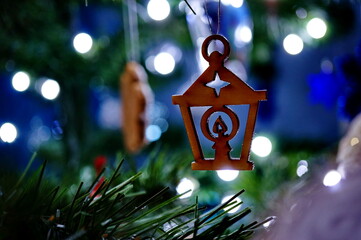 Wooden Christmas decoration in the shape of a candlestick surrounded by little lights, hanging on a Christmas tree