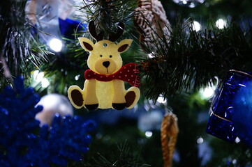 Cute Christmas decoration in a shape of a little white reindeer with a scarf, hanging on a Christmas tree