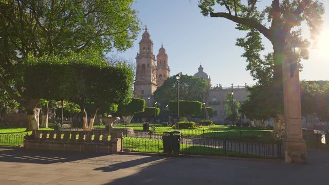 Green Park and Cathedral in Marelia, Michoacan, Mexico. Magnificent morning view of city center in Morelia. Sun breaks through the tree illuminating park and the ancient cathedral