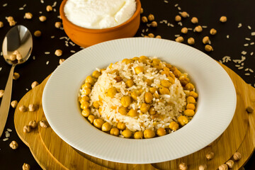 Traditional Turkish Rice Cooked With Chickpea on black background with yoghurt.