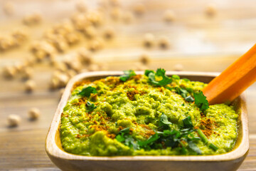 Homemade chickpea hummus with herbs in square bamboo wooden bowl, carrot stick