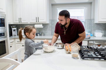 Dad teaching toddler daughter how to cook in home kitchen