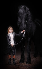 Fototapeta na wymiar Little blonde girl next to a Friesian stallion with a long mane