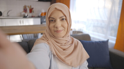 Muslim woman in hijab takes selfie with her mobile phone, laughs, teases, kisses. Front camera...