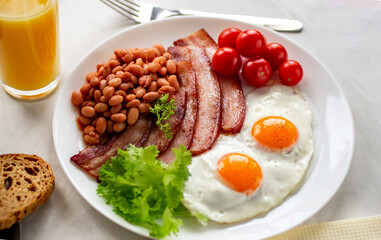 Hearty breakfast with scrambled eggs, bacon, beans, cherry tomatoes, homemade bread, orange juice on a concrete countertop. English breakfast concept. side view