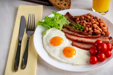 Hearty breakfast with scrambled eggs, bacon, beans, cherry tomatoes, homemade bread, orange juice on a concrete countertop. English breakfast concept.