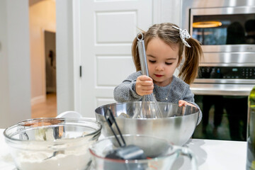 Toddler girl mixing in bowl with wire whisk 