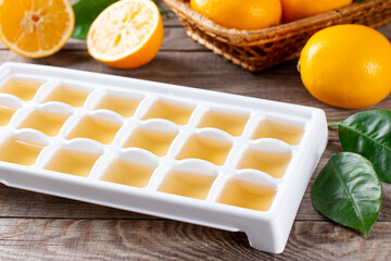 Freezing lemon juice in cubes in a tray with fresh lemons on a wooden table