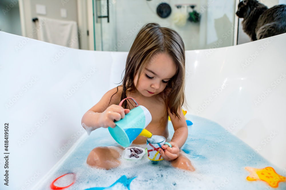 Wall mural happy toddler girl playing with toys in bathtub