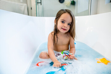 Happy toddler girl playing with toys in bathtub 