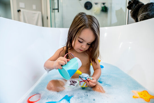 Happy toddler girl playing with toys in bathtub 