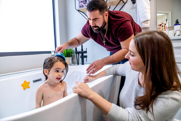 Mother and father bathing toddler daughter together in bathtub