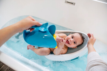 Woman bathing happy baby in bathtub