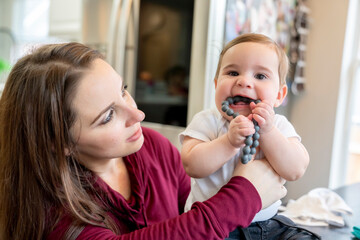 Obraz na płótnie Canvas Teething baby boy sitting on table held by mom