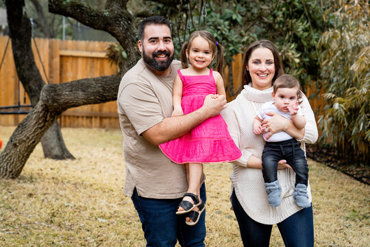 Portrait Of Happy Latinx Family With Baby And Toddler In Their Back Yard