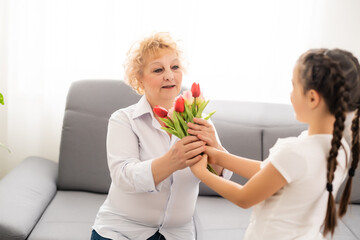 Little beautiful granddaughter gives her grandmother a bouquet of pink tulips. The concept of family, respect, generation, mother, upbringing