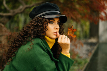 The brooding girl with long curly hair looks in the distance with beautiful eyes the color of her green coat. High quality photo - 418426596