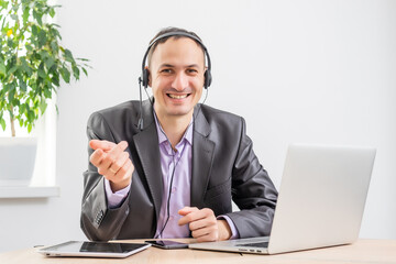 Man working in the office from dawn to dusk. Communication via the Internet. Young businessman using tablet laptop and headphones phone connecting wi-fi. Sunset light. Negotiations on line.