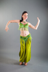 beautiful brunette girl in green belly dance costume smiles at camera in studio