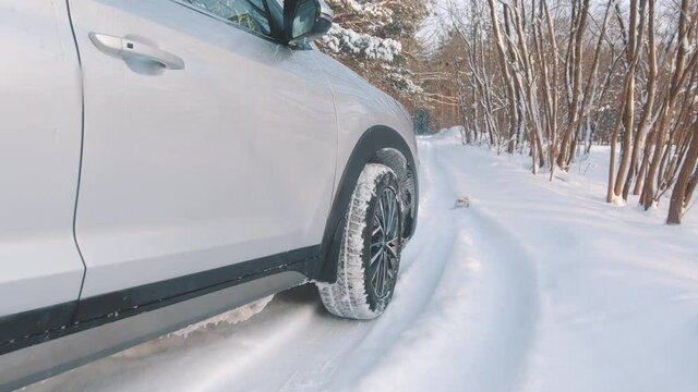 Close up on the car slowly driving on the road covered in the snow with winter tires . High quality 4k footage