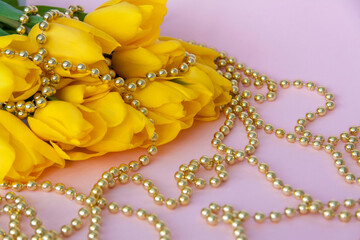 A bouquet of fresh yellow tulips. A bouquet of tulips on a pink background with a scattering of gold beads. Spring flowers in the interior. The concept of spring or holiday, March 8, 